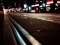 Nocne miasto, światła samochodów i neonów tworzą rozmyty obraz, jakby z powodu kurzej ślepoty. Trolejbusowe szyny błyszczą w ciemności.