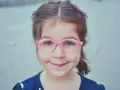 Uśmiechnięta dziewczynka w okularach, z kolorowymi spinkami we włosach, mruganie oczami u dziecka jest urocze.