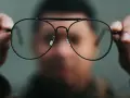 Osoba trzyma przed twarzą okulary, które sprawiają, że świat wygląda inaczej. Nowe okulary dziwne widzenie.