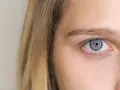 Zbliżenie na niebieskie oko dziewczyny z blond włosami. Powiększone źrenice sugerują zaciekawienie lub zaskoczenie.