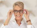 Uśmiechnięta kobieta poprawia okulary z soczewkami pryzmatycznymi.
