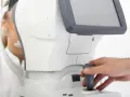 Badanie wzroku pacjentki przy użyciu nowoczesnego sprzętu. Lekarz manipuluje joystickiem, jakby sterował statkiem kosmicznym, a pacjentka patrzy w dal, jakby widziała kolorowy balon.