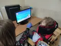 Tyflopedagog w niebieskiej rękawiczce pomaga dziecku w specjalnym foteliku grać w grę na komputerze.