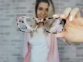 Uśmiechnięta kobieta prezentuje stylowe okulary plusy w różowo-czarnej oprawce.