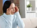 Kobieta zamyka oczy, masując skronie. Silny ból głowy i światłowstręt uniemożliwiają jej normalne funkcjonowanie.