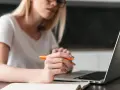 Kobieta pisze przykładowe uzasadnienie wniosku o przyznanie pomocy zdrowotnej na okulary, korzystając z laptopa i notatnika.