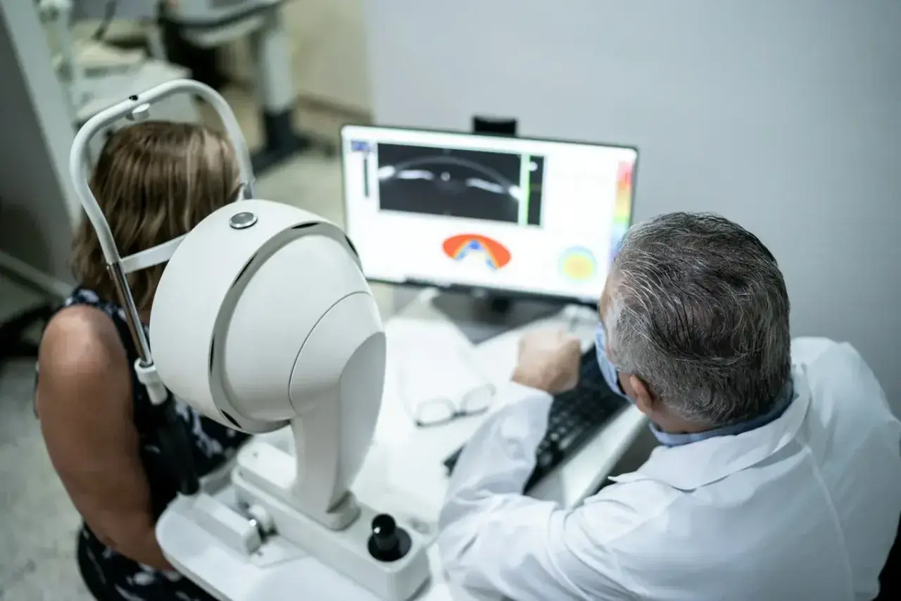 Lekarz omawia z pacjentką wyniki badania oka, analizując obraz na monitorze. W tle widoczny sprzęt okulistyczny, sugerujący diagnostykę, np. angiografia fluoresceinowa, z uwzględnieniem przeciwwskazań.