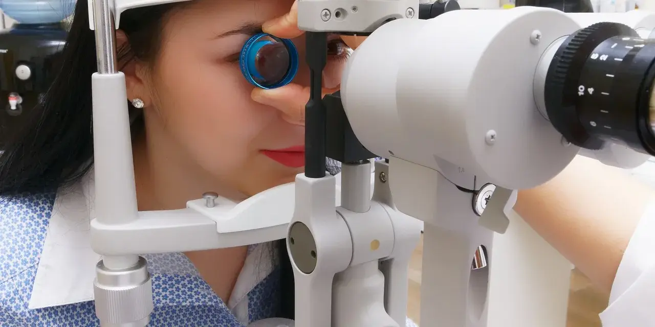 Kobieta podczas badania dna oka przy użyciu specjalistycznego sprzętu. Okulista dokładnie sprawdza wzrok pacjentki.