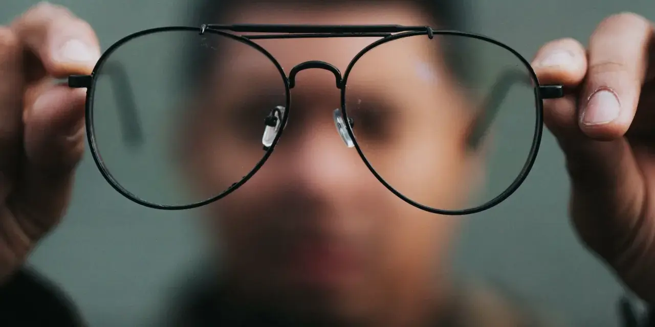 Osoba trzyma przed twarzą okulary, które sprawiają, że świat wygląda inaczej. Nowe okulary dziwne widzenie.