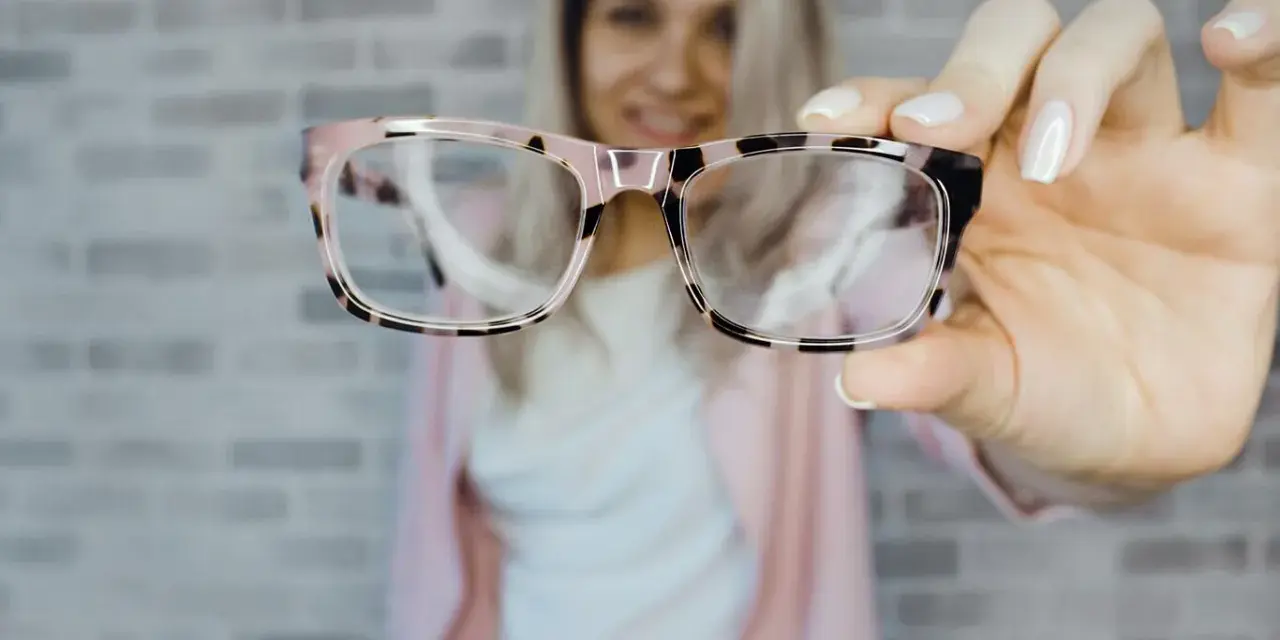 Uśmiechnięta kobieta prezentuje stylowe okulary plusy w różowo-czarnej oprawce.