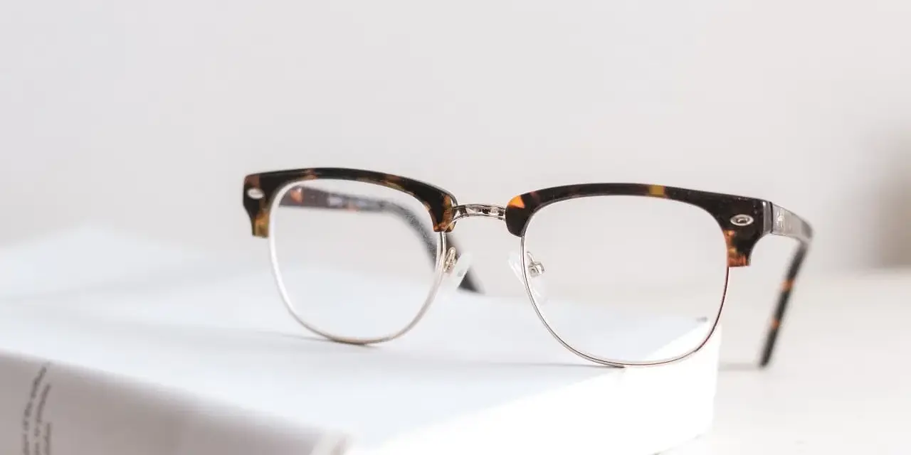 Okulary z oprawkami w stylu clubmaster leżą na białej książce. Czy wada 0.75 to powód, by nosić okulary?