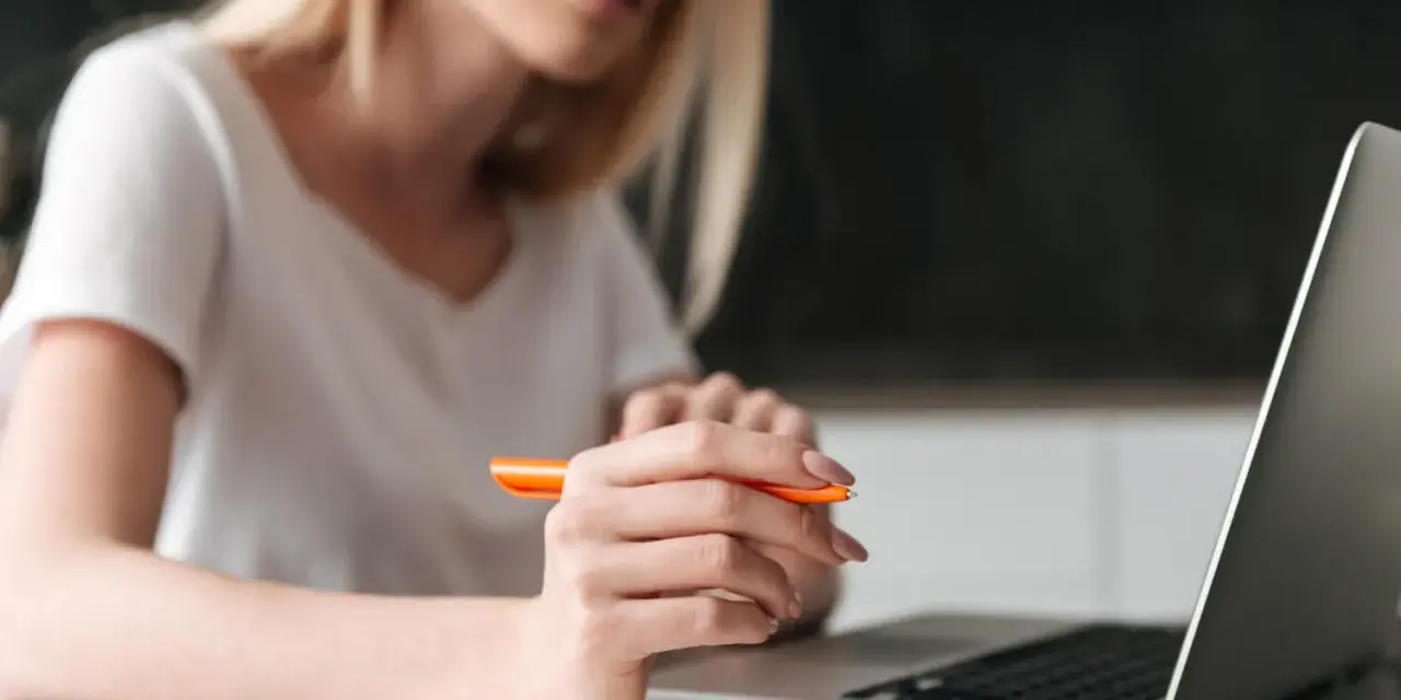 Kobieta pisze przykładowe uzasadnienie wniosku o przyznanie pomocy zdrowotnej na okulary, korzystając z laptopa i notatnika.
