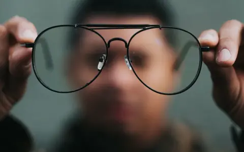 Osoba trzyma przed twarzą okulary, które sprawiają, że świat wygląda inaczej. Nowe okulary dziwne widzenie.