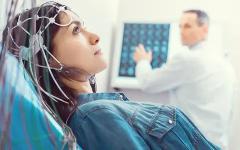 Kobieta z elektrodami na głowie podczas badania VEP. Lekarz analizuje wyniki na ekranie.