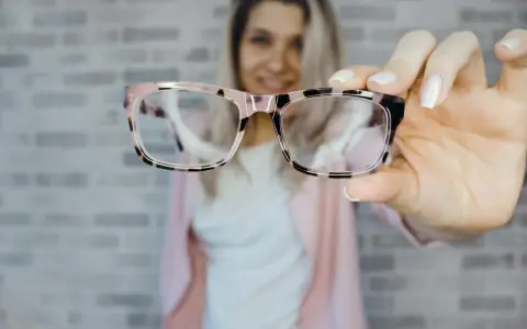 Uśmiechnięta kobieta prezentuje stylowe okulary plusy w różowo-czarnej oprawce.