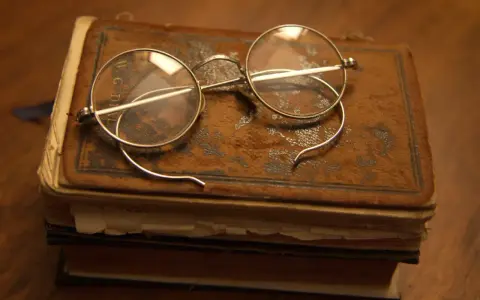 Okulary na starym oprawionym tomie, przypominające czasy, kiedy wynaleziono okulary, by czytać.