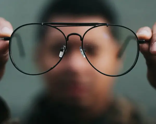Osoba trzyma przed twarzą okulary, które sprawiają, że świat wygląda inaczej. Nowe okulary dziwne widzenie.