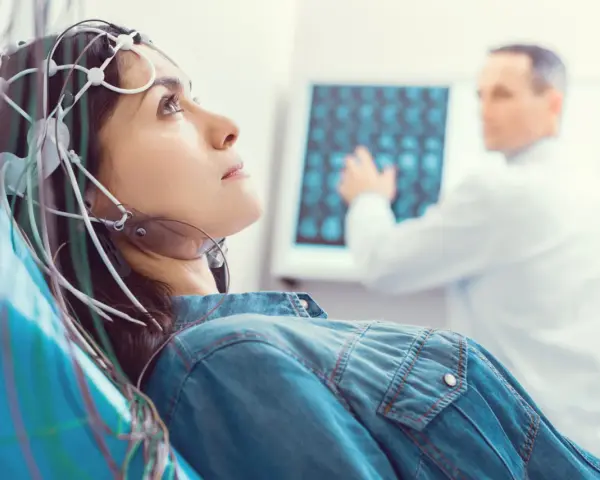 Kobieta z elektrodami na głowie podczas badania VEP. Lekarz analizuje wyniki na ekranie.