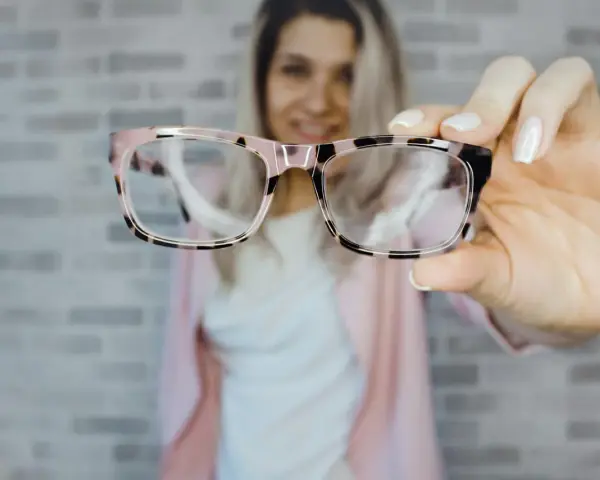 Uśmiechnięta kobieta prezentuje stylowe okulary plusy w różowo-czarnej oprawce.