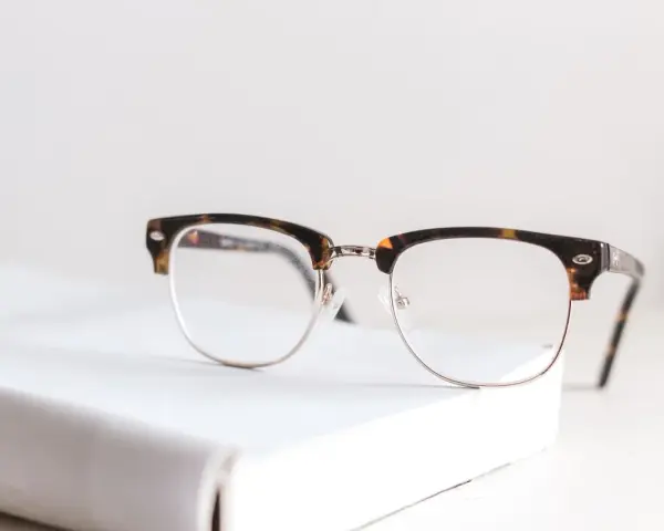 Okulary z oprawkami w stylu clubmaster leżą na białej książce. Czy wada 0.75 to powód, by nosić okulary?