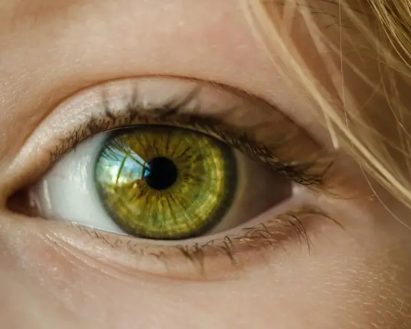 Zielona soczewka oka z refleksami światła, otoczona jasną skórą i blond włosami.