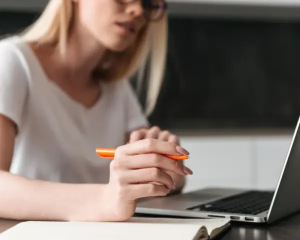 Kobieta pisze przykładowe uzasadnienie wniosku o przyznanie pomocy zdrowotnej na okulary, korzystając z laptopa i notatnika.