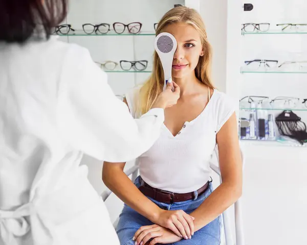 Młoda kobieta przechodzi badanie wzroku. Optometrysta zasłania jej jedno oko przyrządem do cover testu.