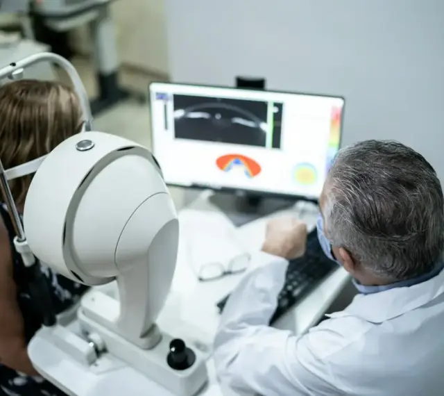 Lekarz omawia z pacjentką wyniki badania oka, analizując obraz na monitorze. W tle widoczny sprzęt okulistyczny, sugerujący diagnostykę, np. angiografia fluoresceinowa, z uwzględnieniem przeciwwskazań.