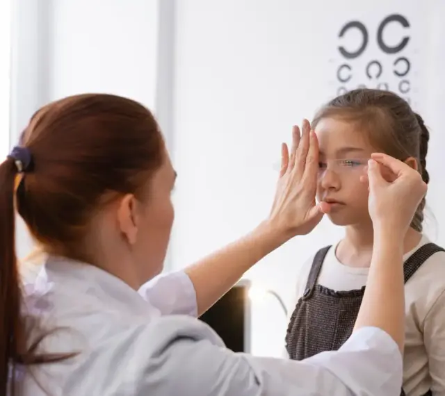 Okulista wykonuje ćwiczenia na poprawę wzroku u dziewczynki, zasłaniając jej jedno oko.