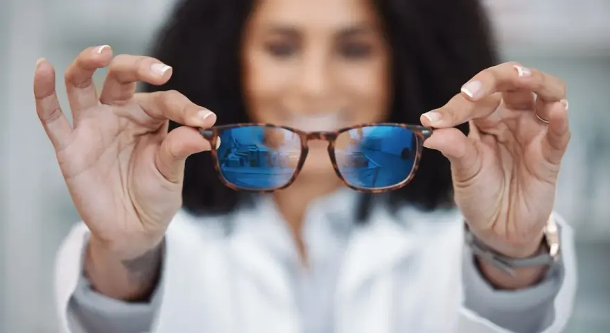 Okulary relaksacyjne wady wzroku? Kobieta w białym kitlu prezentuje okulary z niebieskimi soczewkami, które odbijają wnętrze sklepu.