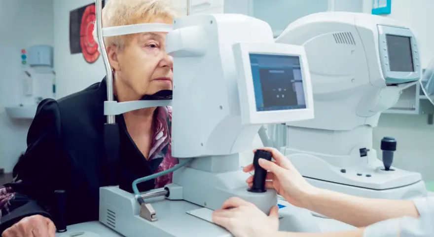Starsza kobieta bada wzrok, skupiając się na ekranie urządzenia. Badanie wykrywa zawężone pole widzenia.