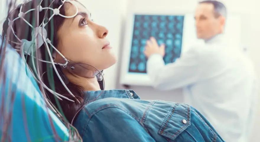 Kobieta z elektrodami na głowie podczas badania VEP. Lekarz analizuje wyniki na ekranie.