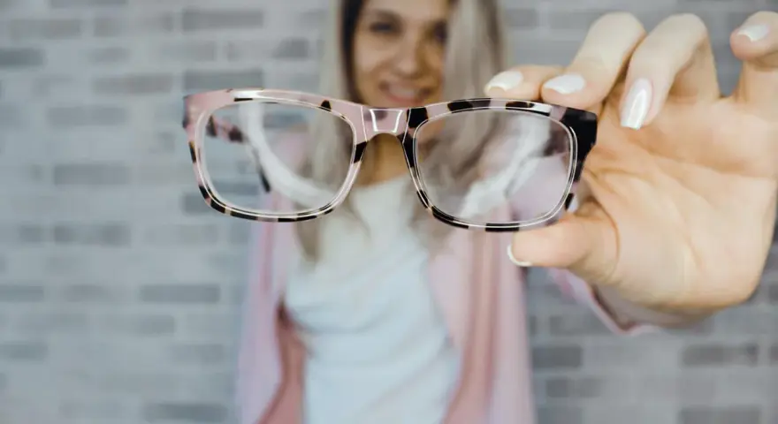 Uśmiechnięta kobieta prezentuje stylowe okulary plusy w różowo-czarnej oprawce.