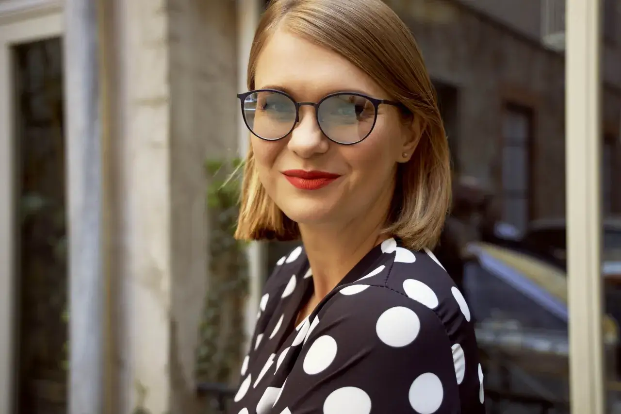 Uśmiechnięta kobieta w okularach fotochromatycznych i sukience w grochy.