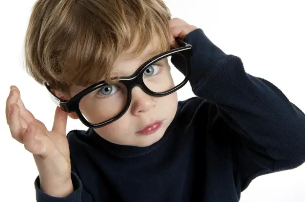 Chłopiec z niebieskimi oczami poprawia okulary, zastanawiając się nad nadwzrocznością u dzieci kiedy okulary są potrzebne.